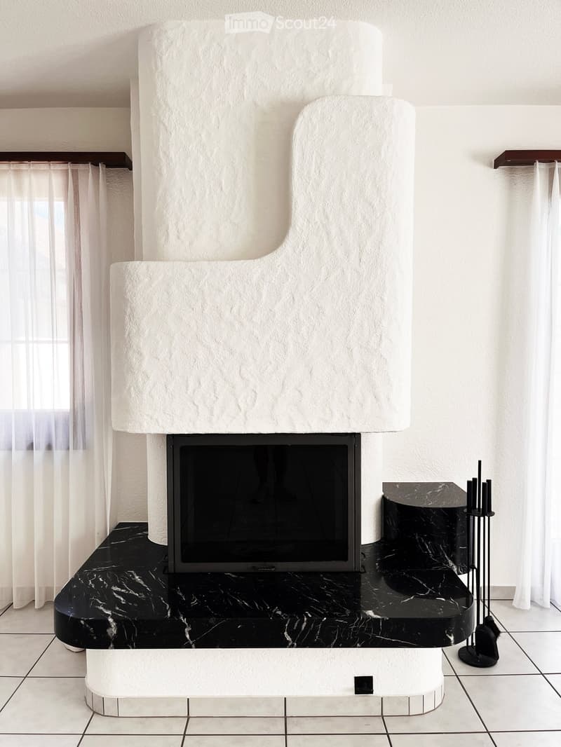 Modern living room with a sleek, white fireplace, black marble flooring, and a small black table with a candle holder nearby.