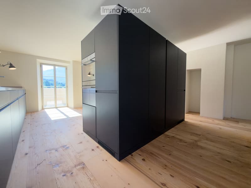 Modern kitchen with dark grey cabinets, light wooden flooring, and a large window offering a scenic view.