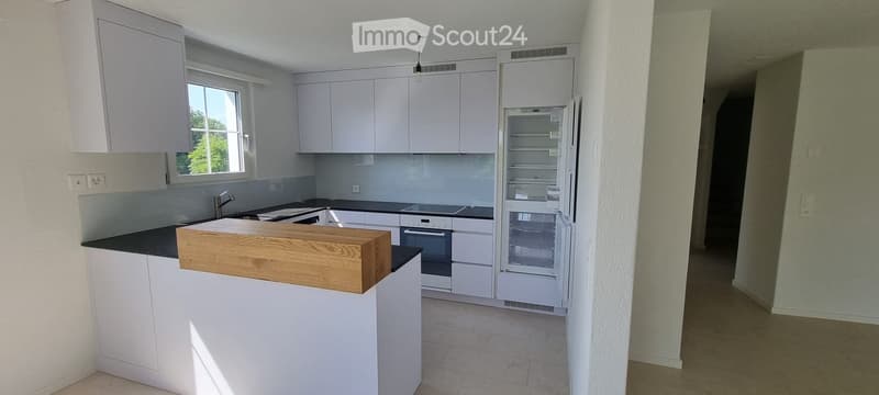 Modern kitchen with white cabinets, black countertops, a wooden island, and stainless steel appliances including a refrigerator, oven, and sink.