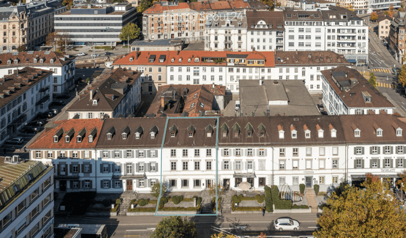 Aerial view of a dense urban area with multiple buildings, featuring a mix of architectural styles and colors, including red-tiled roofs and white facades.