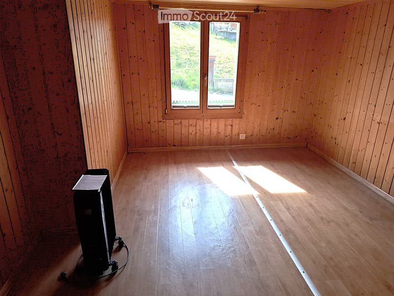 Empty room with wooden walls and floor, two large windows with blinds, and a small black object on the floor.