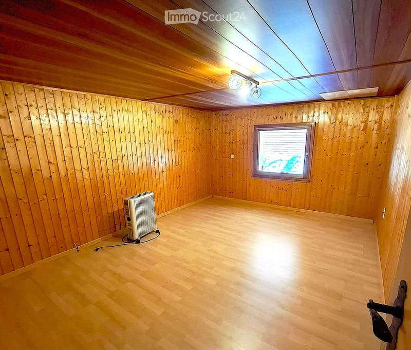 Empty room with wooden walls and floor, a single window, and a small radiator on the left side.