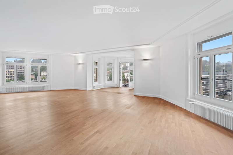 Empty room with light wooden flooring, white walls, and large windows offering a view of the cityscape.