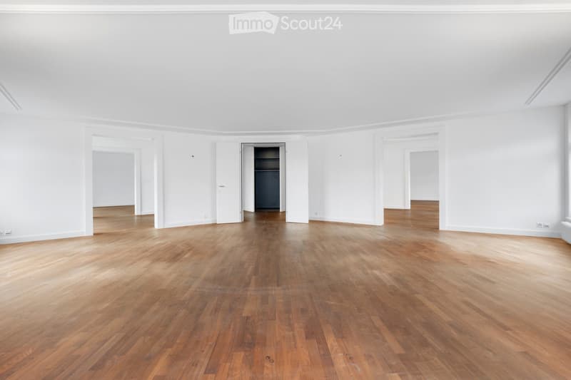 Empty room with light wooden flooring and white walls, featuring several open doorways leading to other spaces.