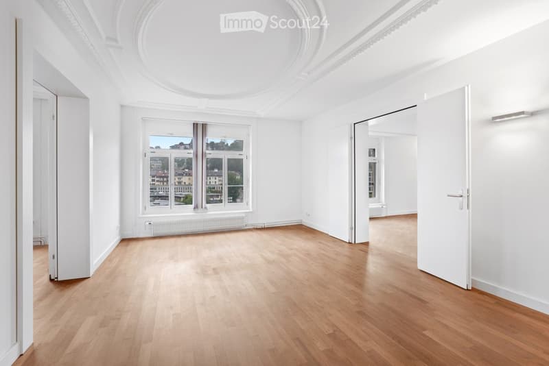 Empty room with wooden flooring, white walls, large windows, and doors leading to other spaces.