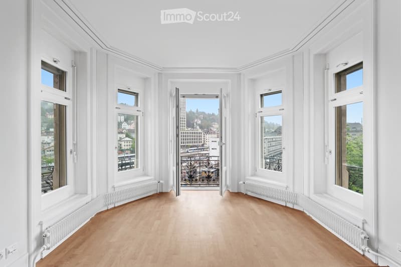 Bright, unfurnished room with wooden flooring, white walls, large windows, and a door leading to a balcony with a city view.