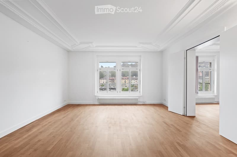 Completely empty room with white walls, wooden floor, large windows, and radiators. No furniture or equipment.