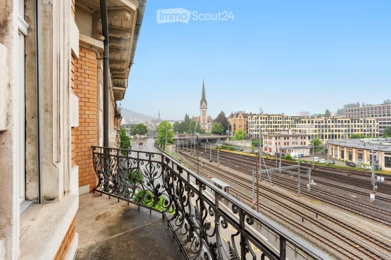 Balcony overlooking a cityscape with train tracks, buildings, and a church spire in the distance.