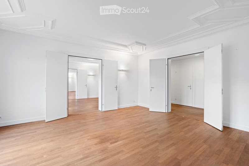 Empty room with light wooden flooring, white walls, and multiple open doors leading to other rooms.