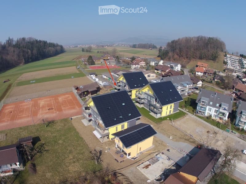 Aerial view of residential buildings, large field, tennis court, solar panels on roofs