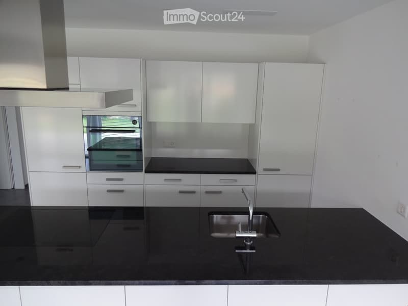 Modern minimalist kitchen with black countertops, white cabinets, oven, dishwasher, kitchen sink, and granite tile backsplash.