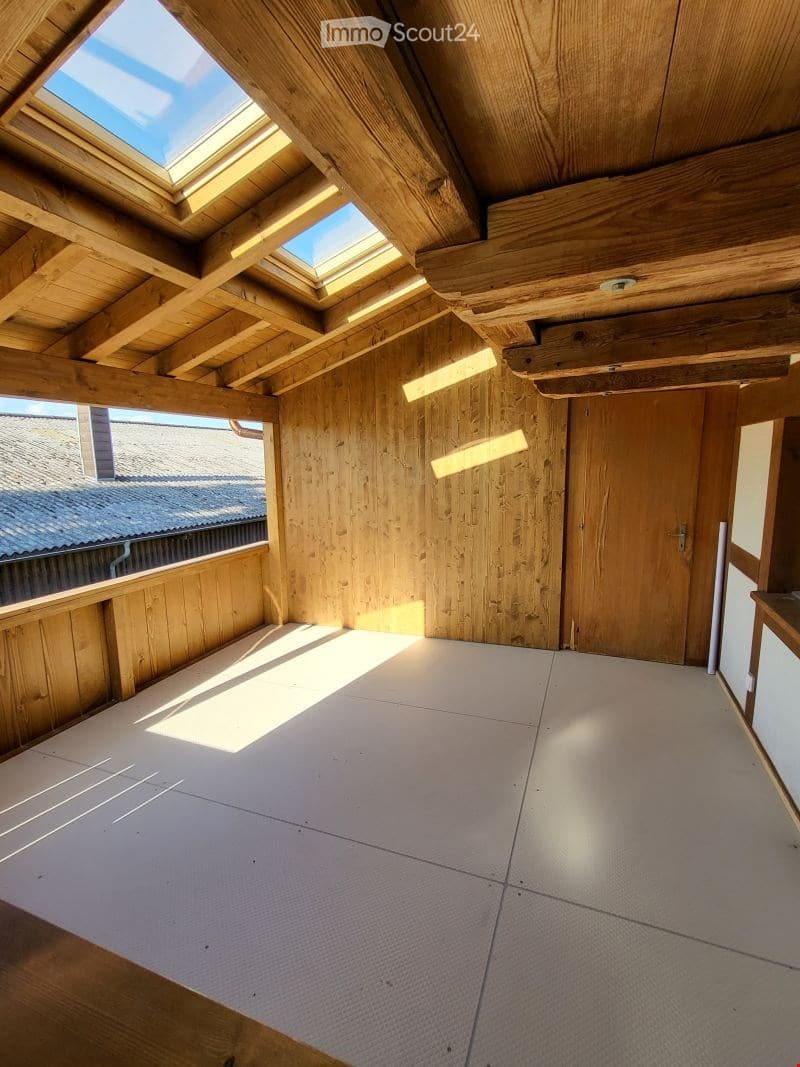 Empty attic space with wooden beams, skylights, and a wooden door. The floor is covered with protective material.