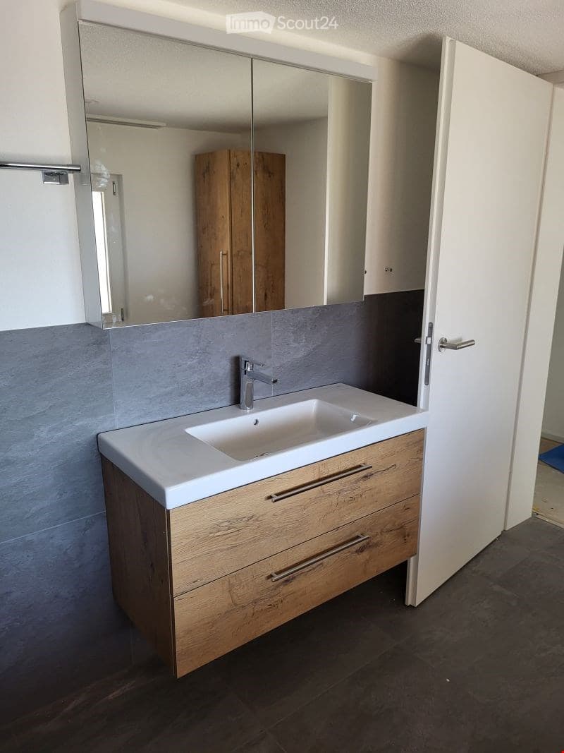 Modern bathroom with a white countertop sink, chrome faucet, large mirror, and wooden cabinet with drawers.