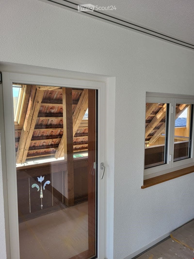 Empty hallway with white walls, a glass door leading to a view of a wooden roof structure, and a window with a wooden sill on the right side.