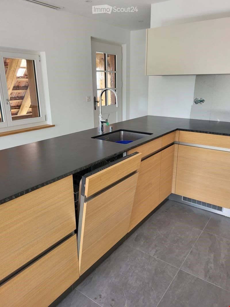Modern kitchen with light wooden cabinets, black countertop, and stainless steel sink.