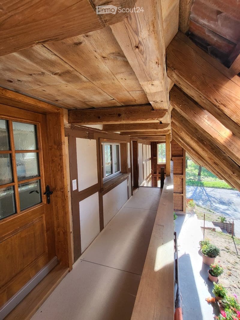Wooden balcony with exposed beams, large windows, and potted plants visible outside.