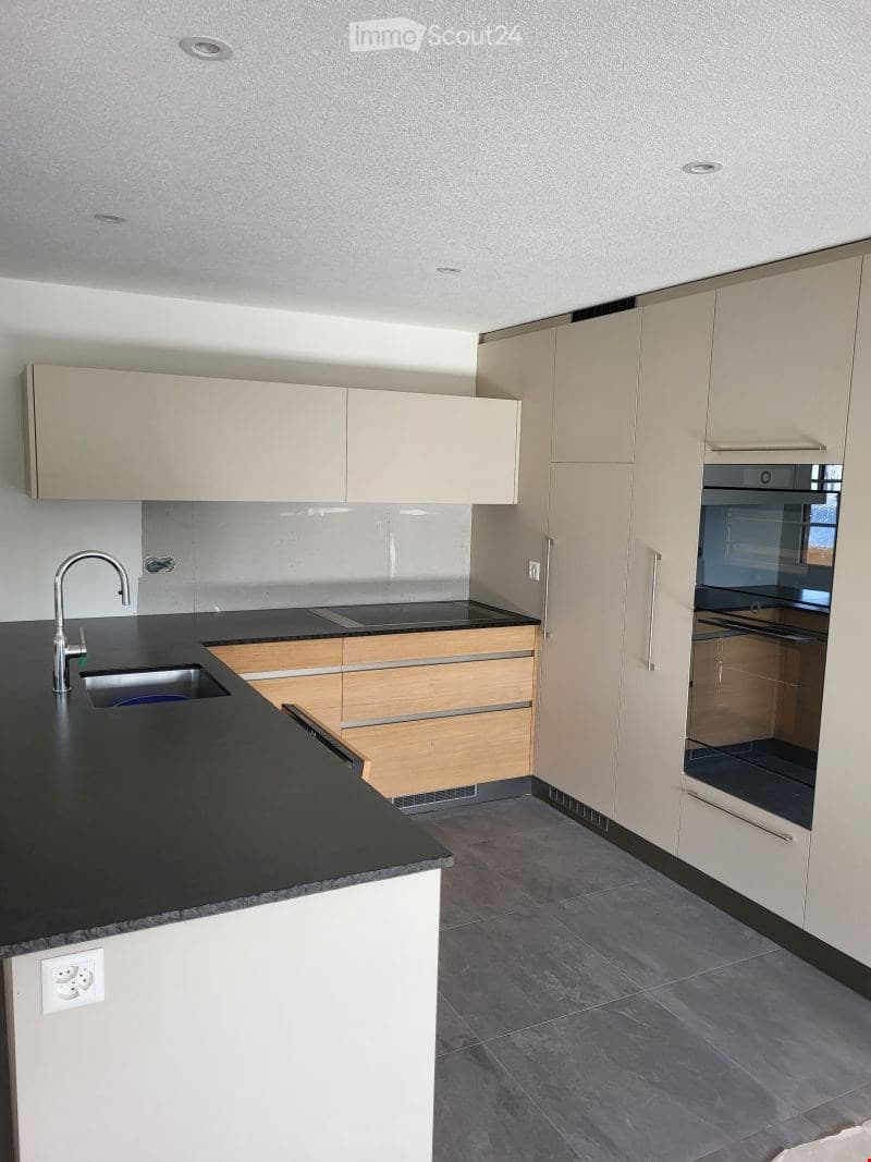 Modern kitchen with light-colored cabinets, black countertop, stainless steel sink and faucet, built-in oven, and wooden drawers.