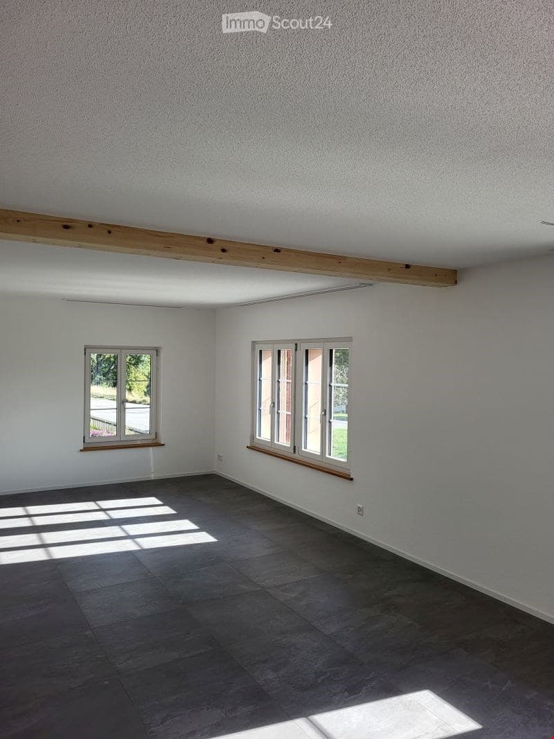 Empty room with white walls, dark tiled floor, and two windows with wooden sills. No furniture or equipment present.