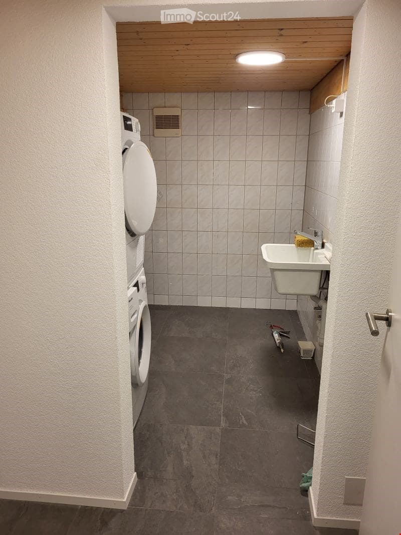 Bathroom with a washing machine, toilet, sink, and tiled walls and floor.