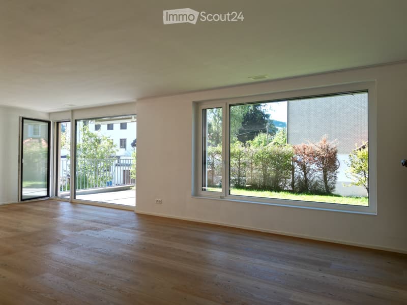Empty room with wooden flooring, large windows, and sliding doors leading to an outdoor area.