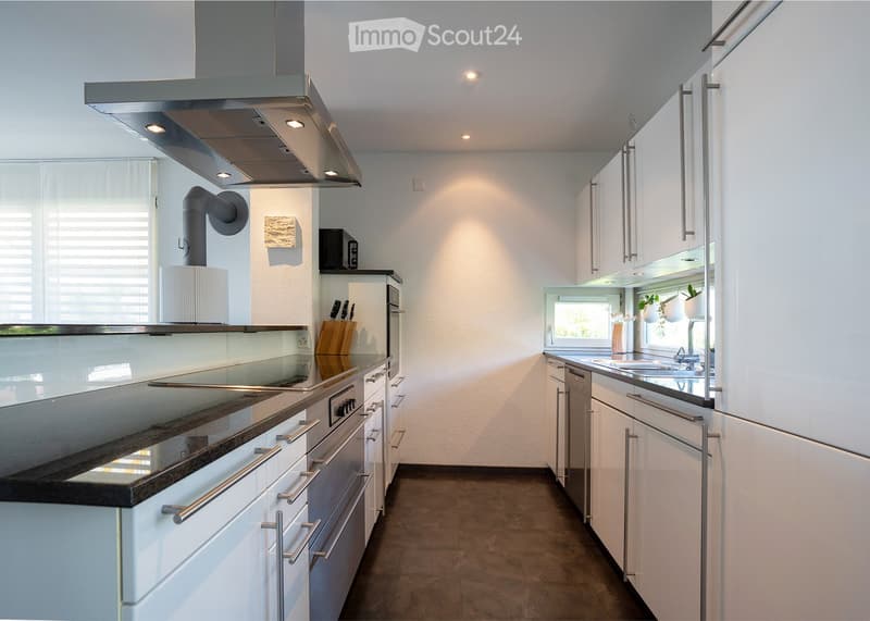 Modern kitchen with white cabinets, stainless steel appliances, and a dark countertop. Features include a built-in oven, refrigerator, sink, and range hood.
