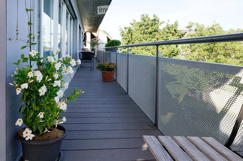 Balcony with wooden decking, metal railing, potted plants, and outdoor seating area.