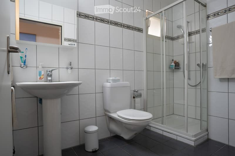 Modern bathroom with white tiles, a sink, toilet, glass-enclosed shower, mirror, and various toiletries.