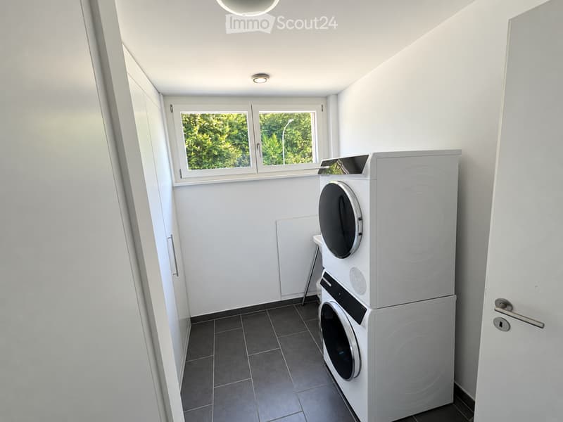 Modern bathroom with white walls, dark tiled floor, and a stacked washing machine and dryer unit.