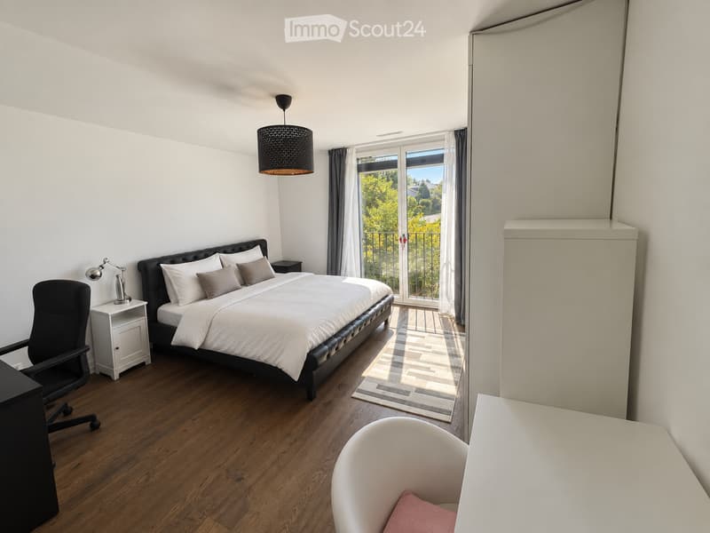 Modern bedroom with a large bed, nightstand, office chair, and a view through large windows.