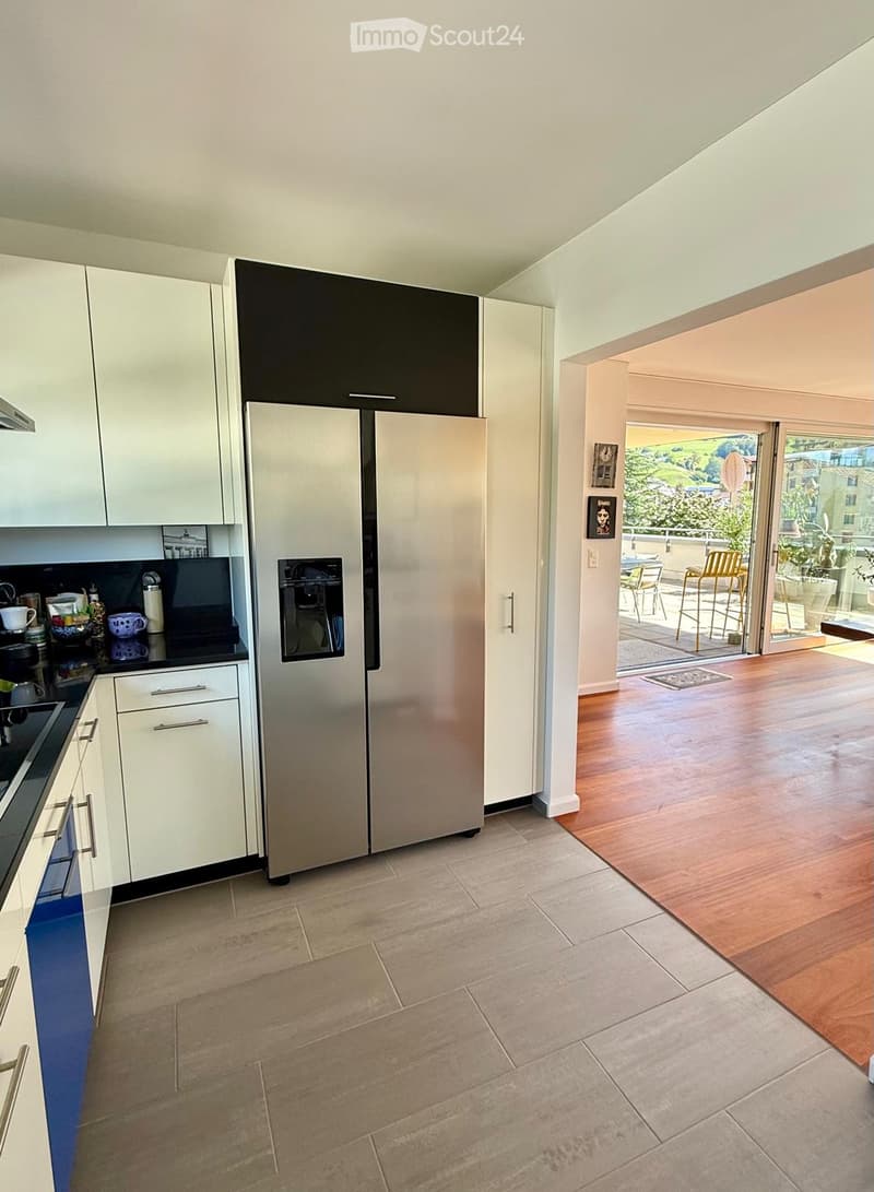 Modern kitchen with white cabinets, stainless steel refrigerator, and a view to a balcony area with outdoor furniture.