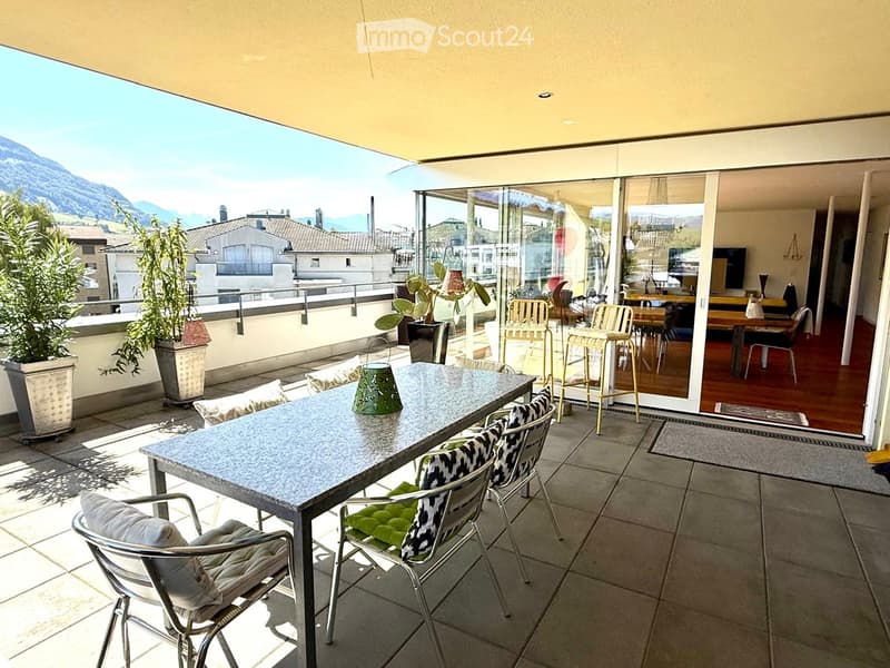 Balcony with a dining table, chairs, and potted plants, offering a scenic mountain view.