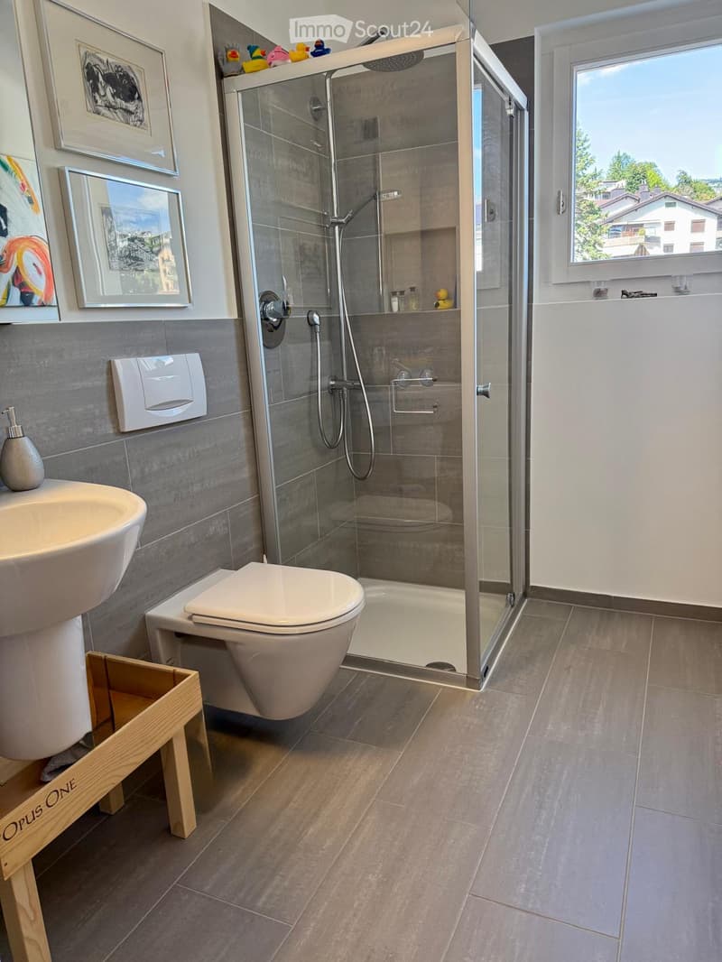 Modern bathroom with a toilet, sink, glass-enclosed shower, and framed artwork on the wall.