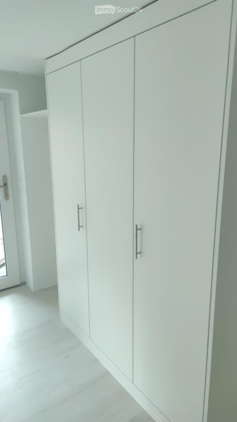 Empty room with white built-in wardrobes, white walls, and a white tiled floor.