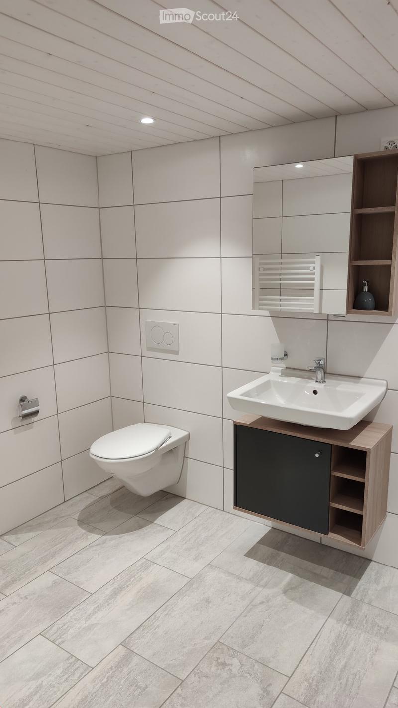 Modern bathroom with white tiles, a floating sink with a wooden cabinet, a toilet, a large mirror, and a towel rack.