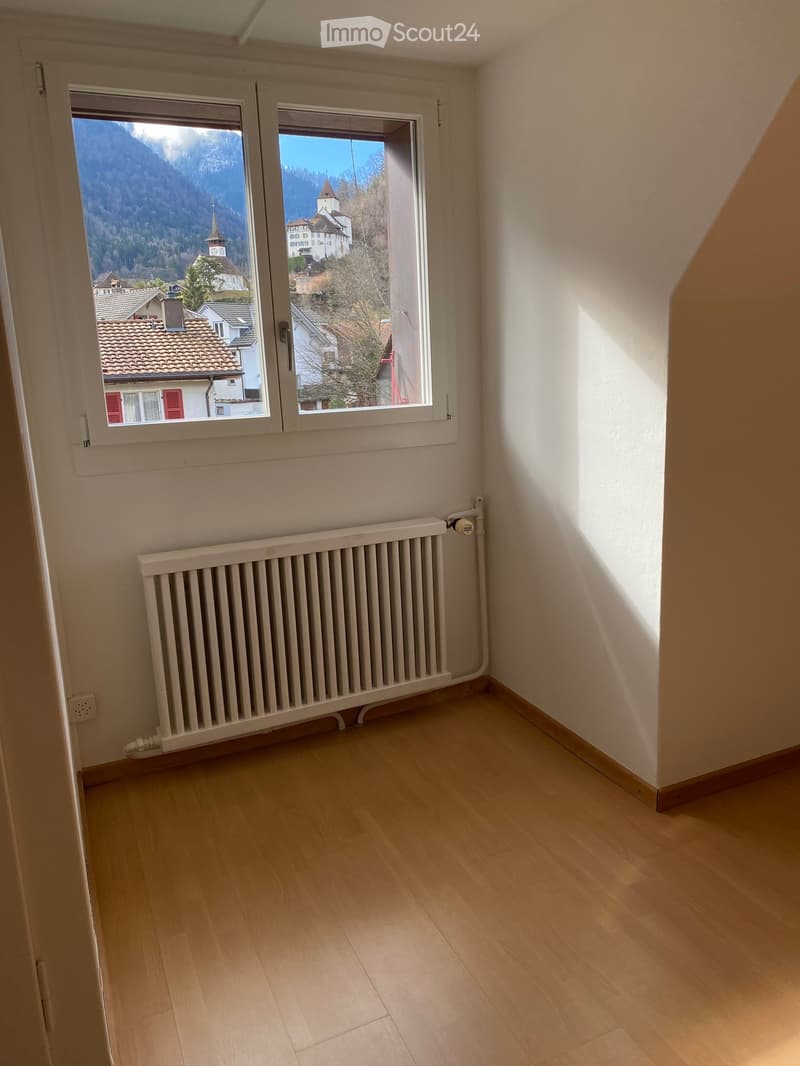 Empty room with wooden flooring, white walls, a radiator, and large windows offering a scenic mountain view.