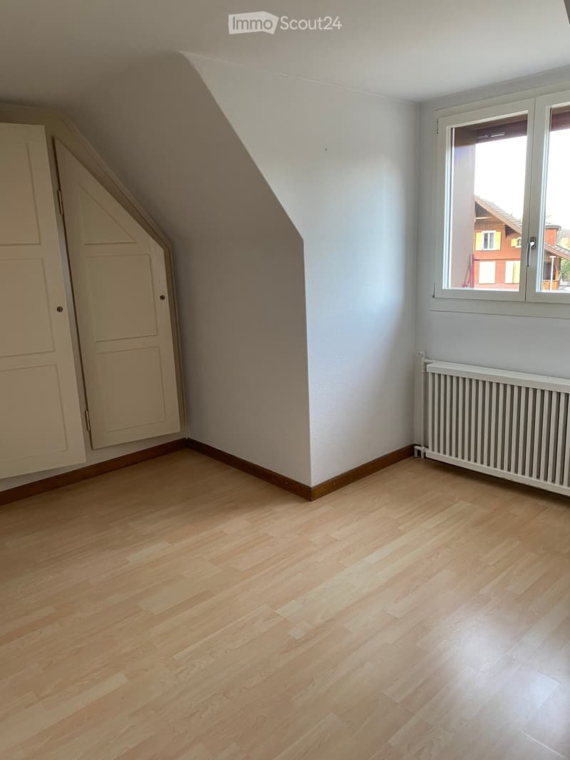 Empty attic room with wooden flooring, white walls, a window, a radiator, and a closet door.