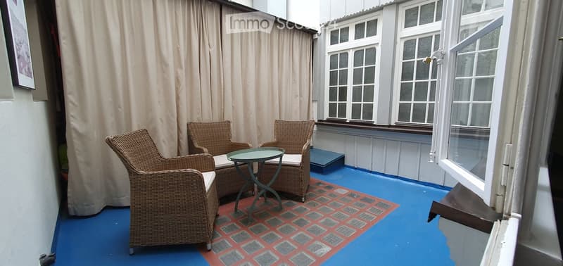 Balcony with blue painted floor, red and grey checkered tile area, wicker chairs, and a small round table.