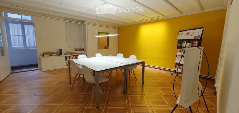 Bright room with wooden flooring, white table and chairs, a cabinet with books, and a screen on a stand.