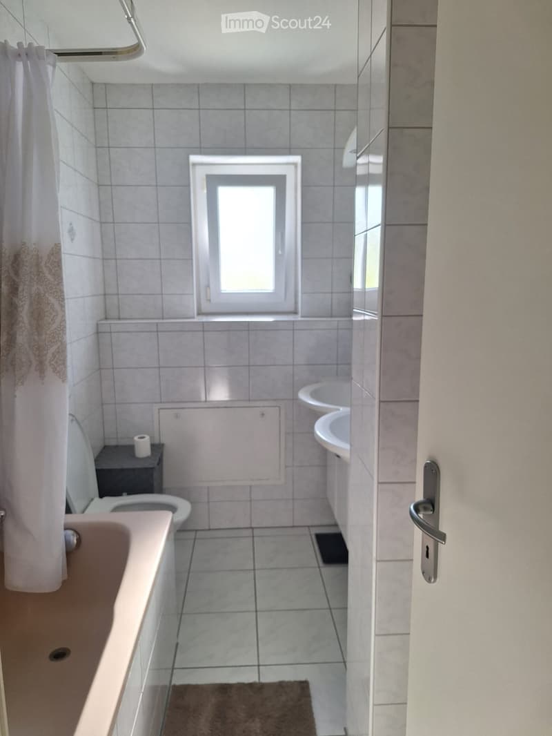 Bathroom with a bathtub, toilet, sink, mirror, and a small window above the toilet. Shower curtain is visible on the left side.
