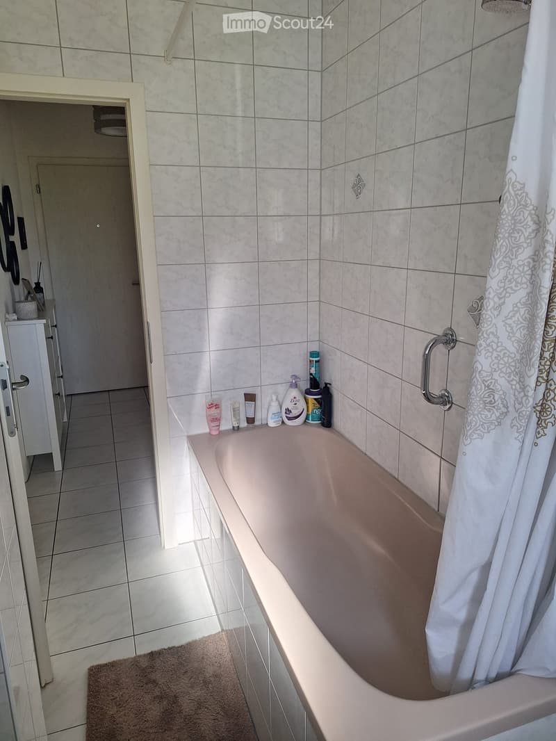 Bathroom with a bathtub, shower curtain, and various toiletries on the edge of the tub. A small cabinet is visible in the background.