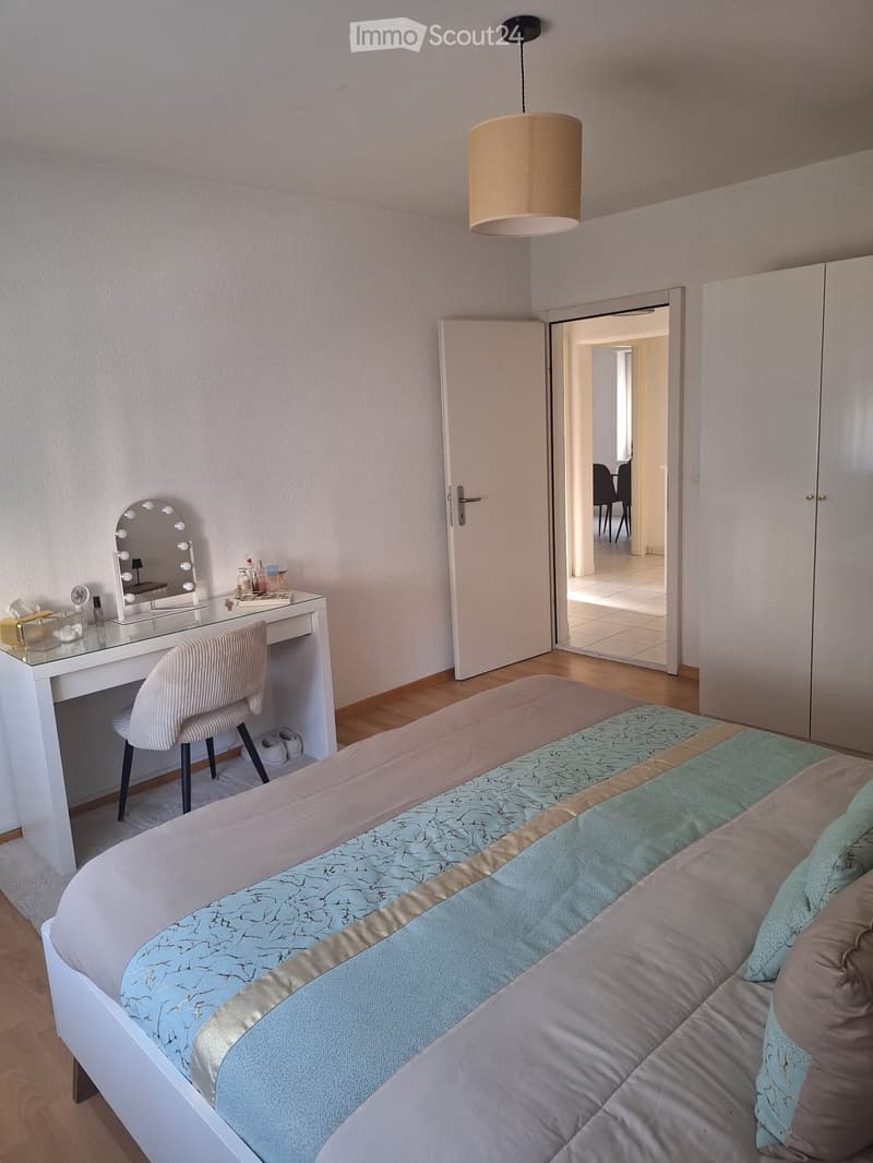 Modern bedroom with a large bed, a vanity desk with a mirror, a chair, and a hanging lamp.