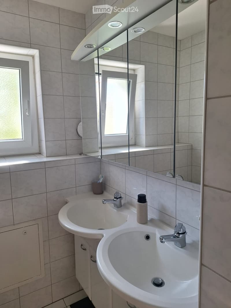 Modern bathroom with double sink, mirrored cabinet, and tiled walls.