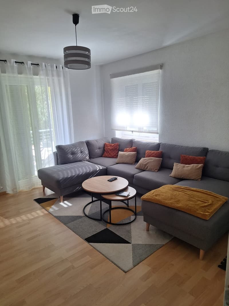 Modern living room with grey sectional sofa, wooden coffee table, small round tables, throw blanket, and decorative pillows.