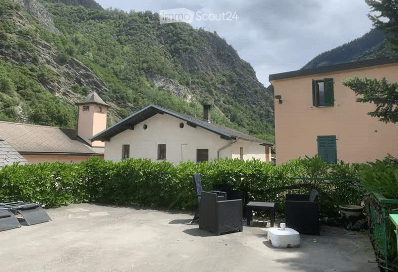 Outdoor patio with a scenic mountain view, featuring a few chairs, a small table, and a stool.