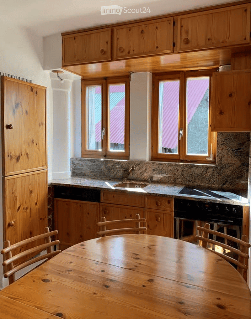 Bright kitchen with wooden cabinets, granite countertop, sink, stove, dishwasher, and a wooden dining table with chairs.