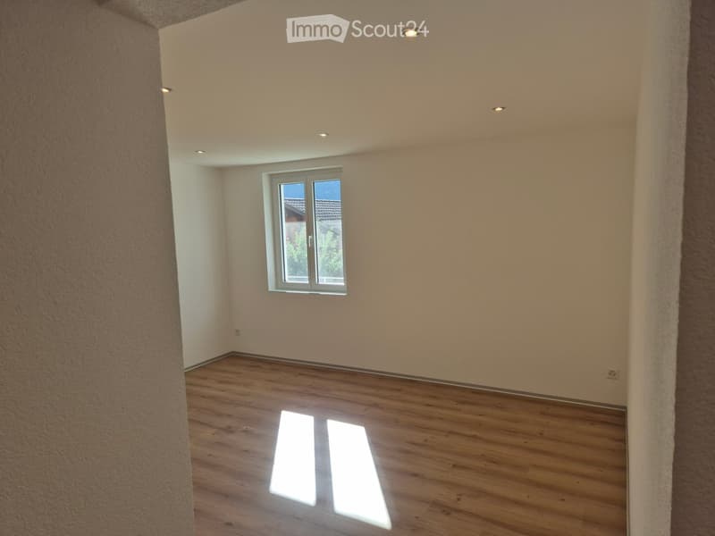 Empty room with wooden flooring, white walls, and a single window with white frame. The room has recessed ceiling lights and appears to be a blank canvas for furnishing.