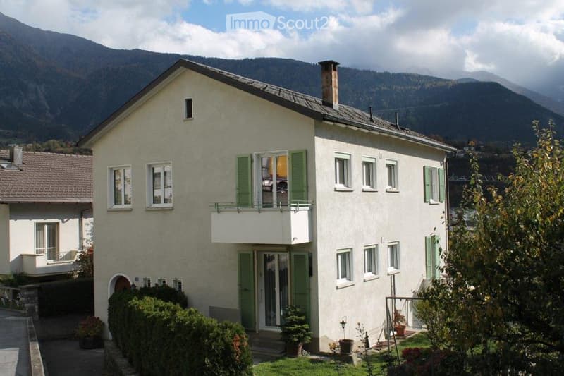 Two-story house with white walls, green shutters, and a balcony overlooking a scenic mountain view.