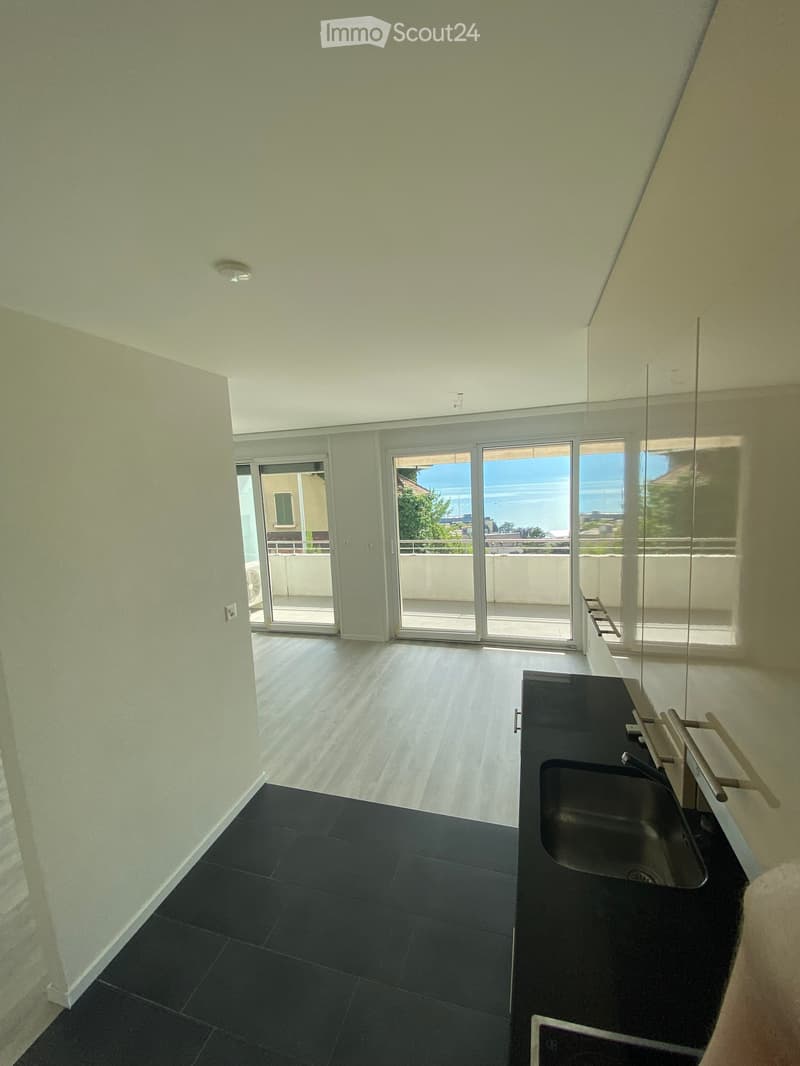 Empty kitchen with black countertops, a sink, and large sliding glass doors leading to a balcony with a sea view.