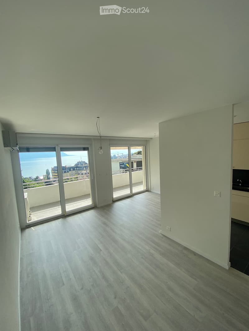 Empty room with light green walls, light wooden flooring, and large sliding glass doors leading to a balcony with a sea view.