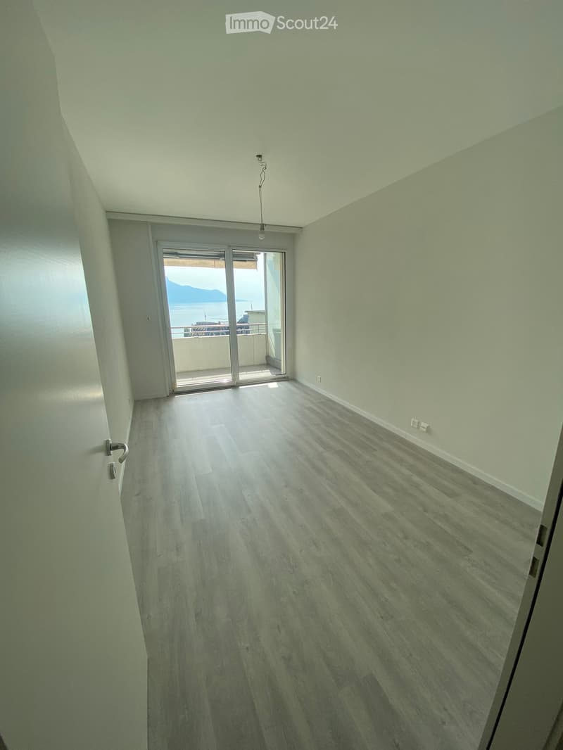 Empty room with light green walls, wooden flooring, and a sliding glass door leading to a balcony with a sea view.